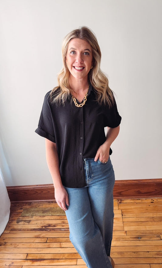 Woman wearing a black shirt and blue jeans standing in a room with wooden flooring.