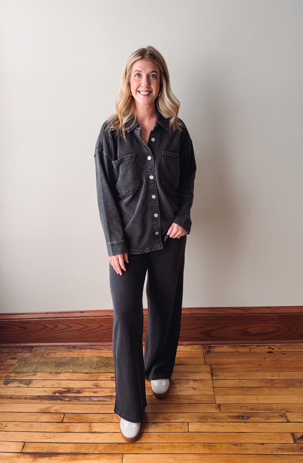 Woman wearing a dark denim shirt and black pants standing on a wooden floor.