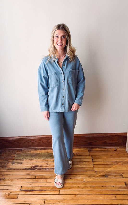 Woman wearing a blue denim outfit standing on a wooden floor with a white wall background