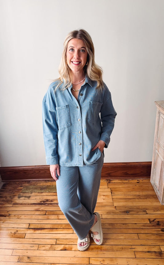 Woman wearing a light blue denim outfit standing on a wooden floor.
