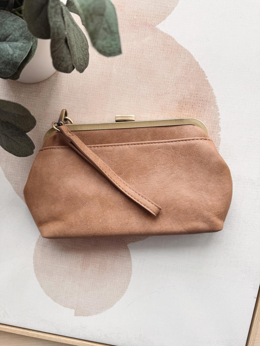 Brown handbag on a white surface with a plant in the background