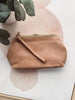 Brown handbag on a white surface with a plant in the background