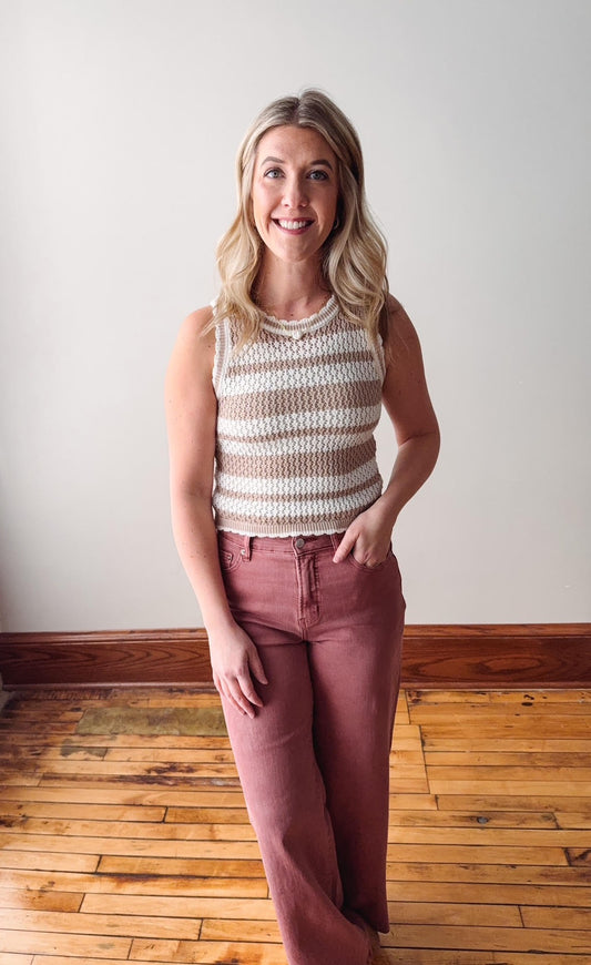 Woman wearing a striped sleeveless top and pink pants standing on a wooden floor.