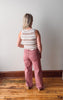 Person wearing a striped sleeveless top and pink pants standing in a room with wooden flooring and a white wall.