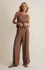 Woman wearing a brown sleeveless top and wide-leg pants on a beige background