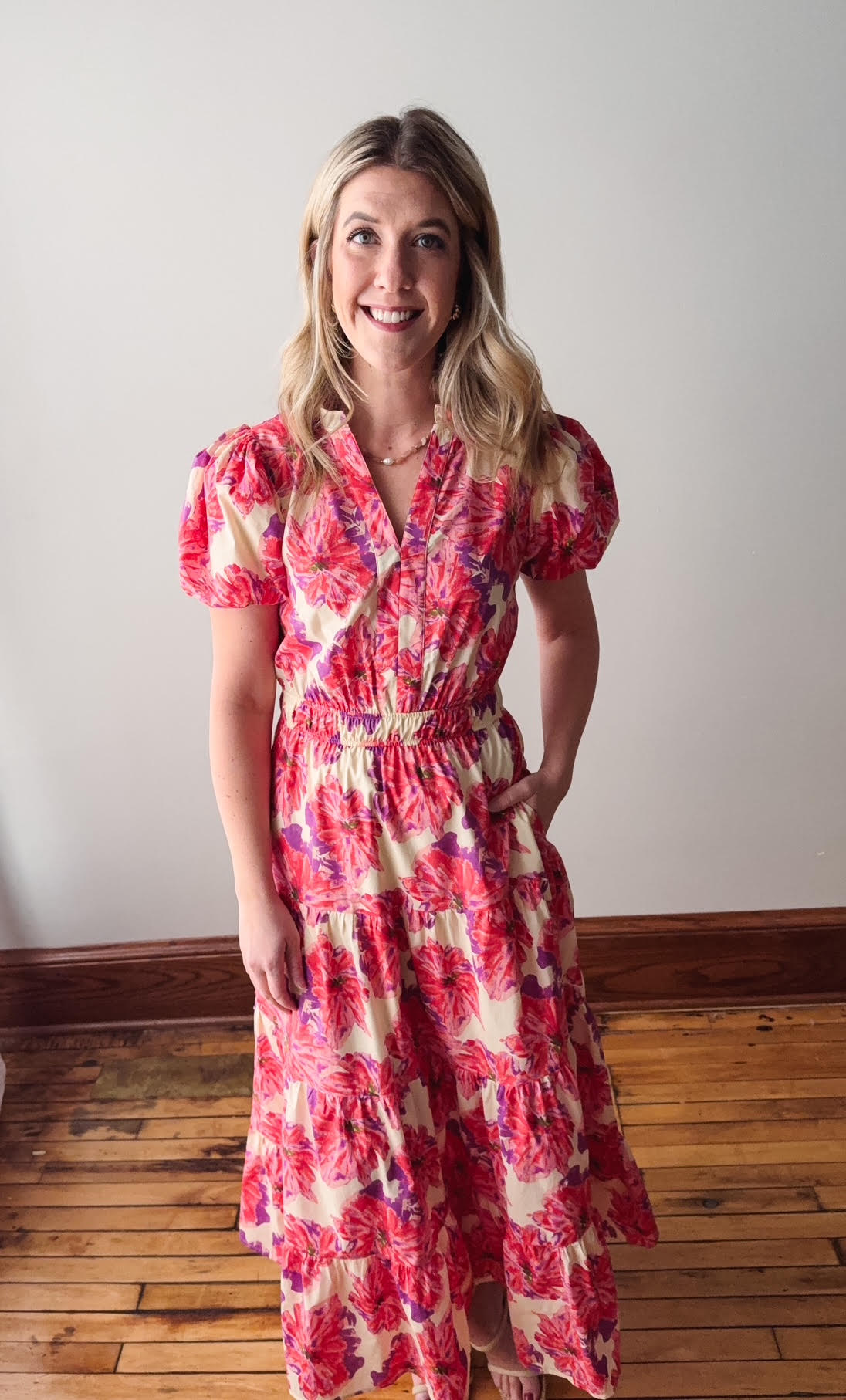 Woman wearing a red floral dress standing on a wooden floor with a white wall background