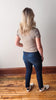 Person wearing a beige top and blue jeans standing on a wooden floor with a white wall background