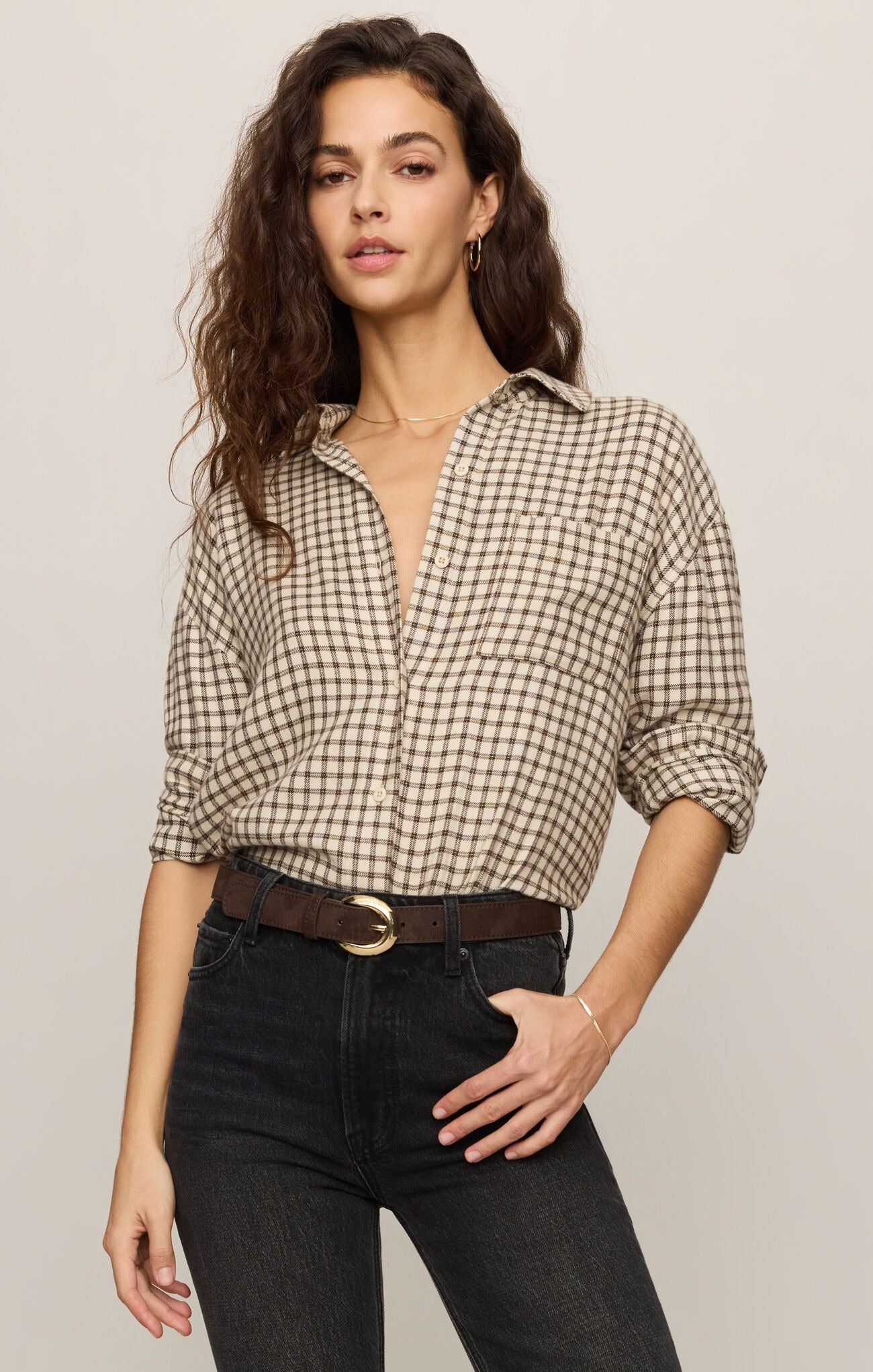 Woman wearing a checkered shirt and black pants against a plain background
