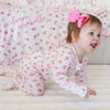 Baby in a floral outfit with a pink bow sitting on a white surface.