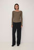 A model stands against a plain white studio background wearing a brown and beige horizontally striped long-sleeve boat-neck top, black wide-leg trousers, and black shoes.