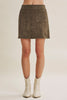 A model from the waist down wearing a dark brown suede mini skirt with front button details and flap pockets, paired with off-white cowboy boots, against a light beige studio background.