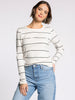 Woman wearing a white sweater with black stripes and blue jeans on a light gray background