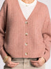 Pink knitted cardigan worn by a person on a plain background