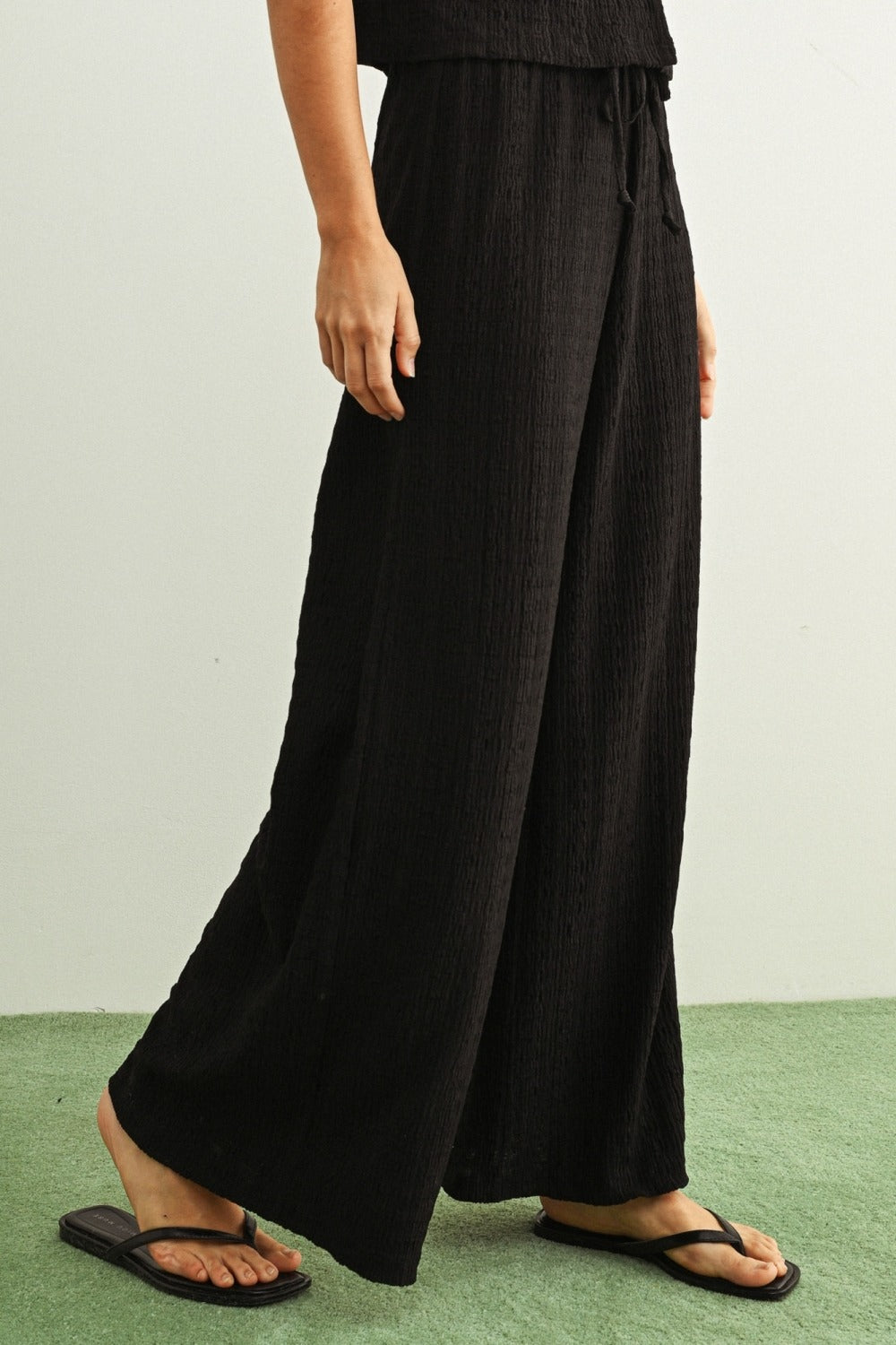 Person wearing black wide-leg pants on a green floor with a white wall background