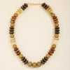 A beaded necklace made of flat, disc-like stone beads in earthy brown, tan, cream, and dark brown tones, with a gold clasp, photographed on a plain light background.