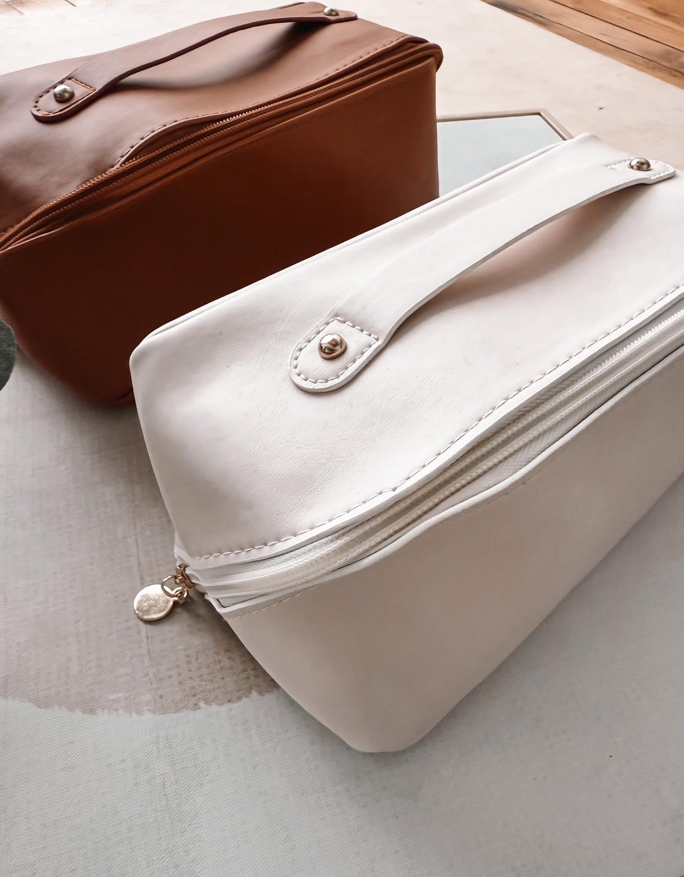 White clutch bag with gold zipper and hardware on a light surface.