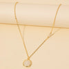 A delicate gold chain necklace with a small round white stone pendant, displayed on a cream-colored background.