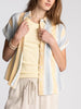 Woman wearing a striped shirt over a yellow top with beige pants on a light gray background