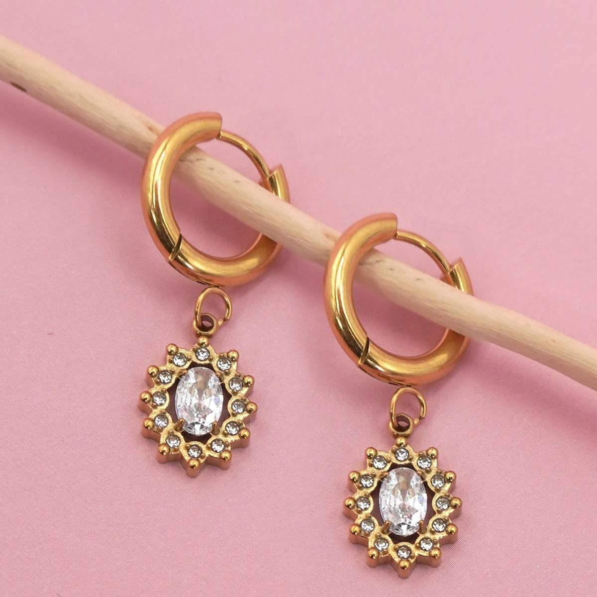 Gold hoop earrings with gemstone pendants on a pink background