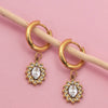 Gold hoop earrings with gemstone pendants on a pink background