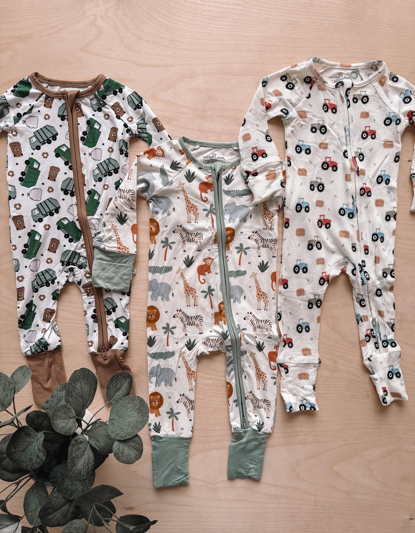 Three baby onesies with different patterns on a wooden surface.