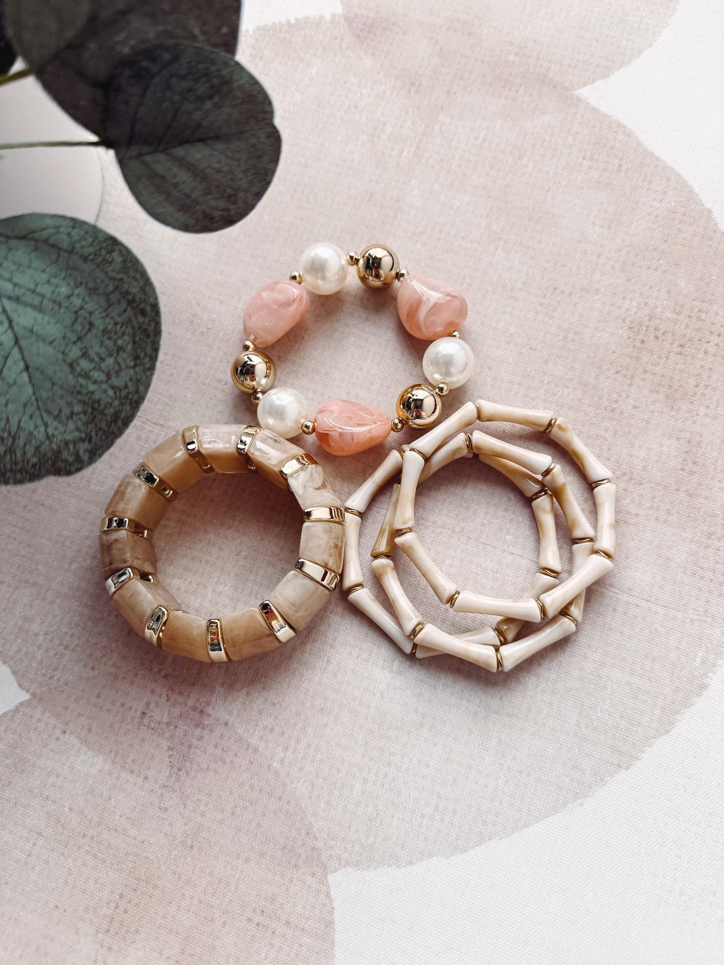 Three beaded bracelets on a textured surface with green leaves in the corner