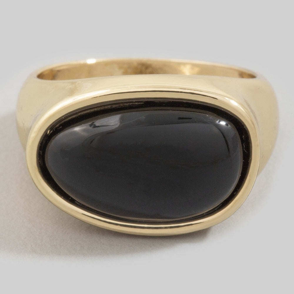 Gold ring with a black stone on a light gray background