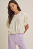 Woman wearing a light-colored blouse and lavender pants against a plain background