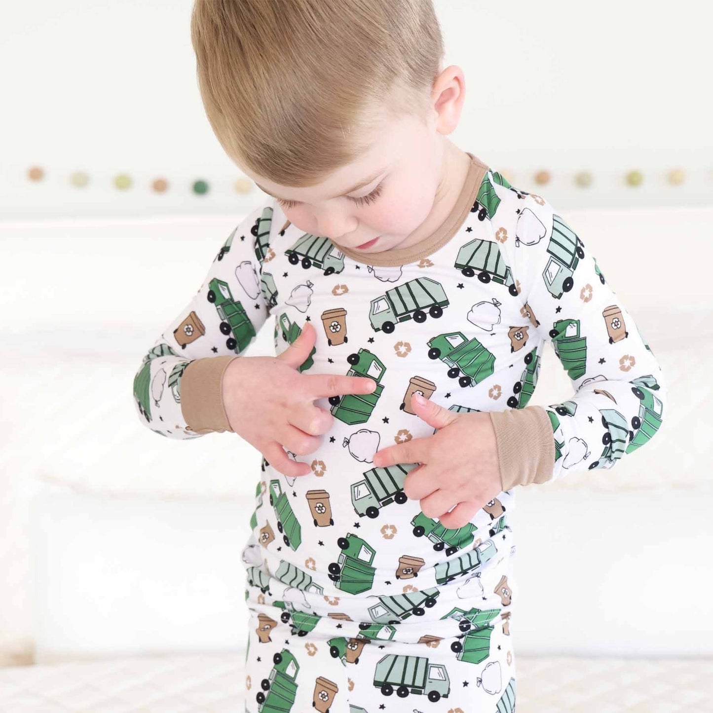 Child wearing a pajama set with green truck pattern on a white background