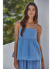 Woman wearing a blue dress standing against a white wall with greenery in the background