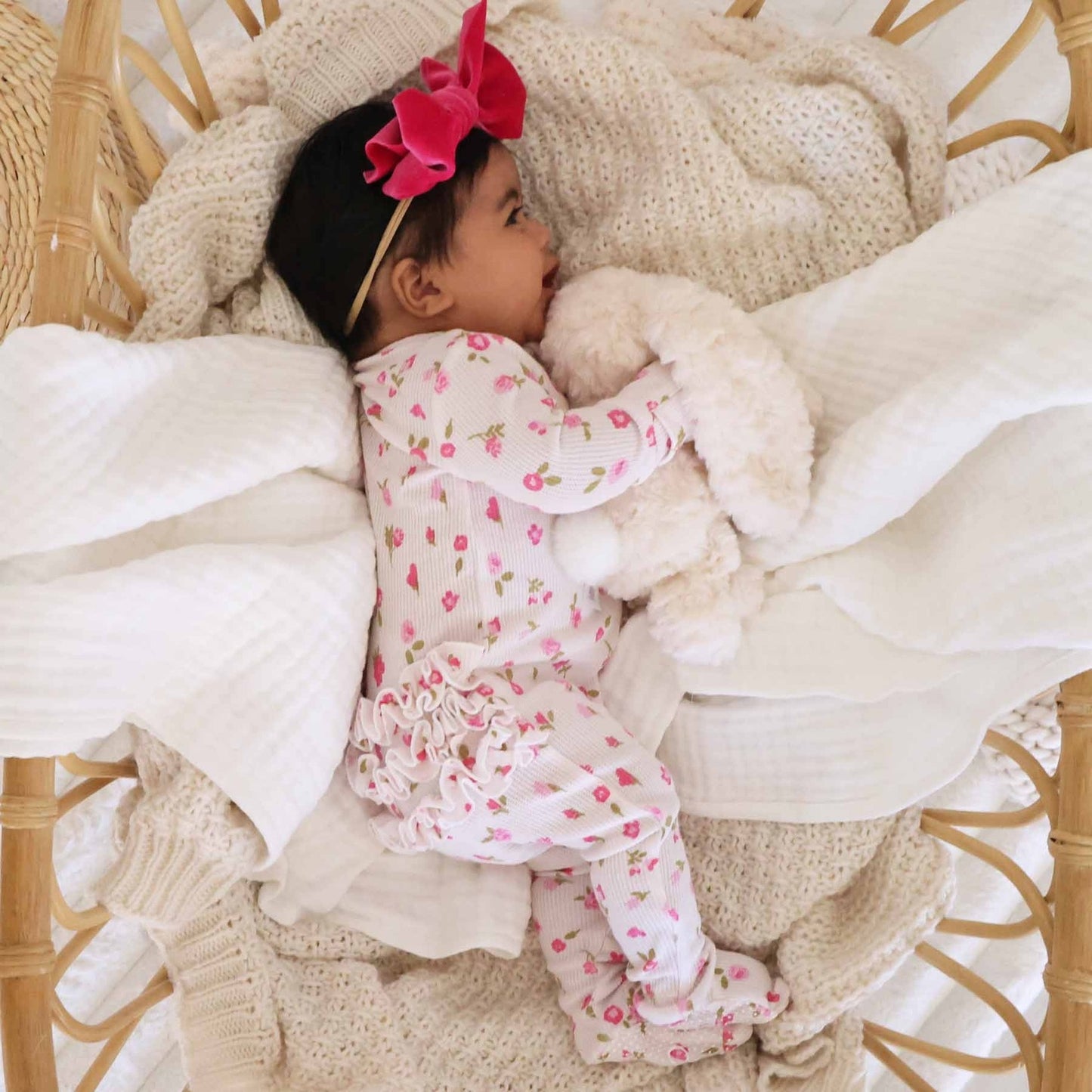 Baby in a floral outfit lying on soft blankets with a pink bow.