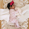 Baby in a floral outfit lying on soft blankets with a pink bow.