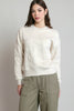A woman modeling a cream-colored crewneck sweatshirt with tonal floral embroidery on the front and sleeves, paired with olive green cargo pants, against a neutral gray background.
