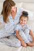 A woman and a young girl sitting together on a white bed, both wearing matching light blue and white floral pajamas.