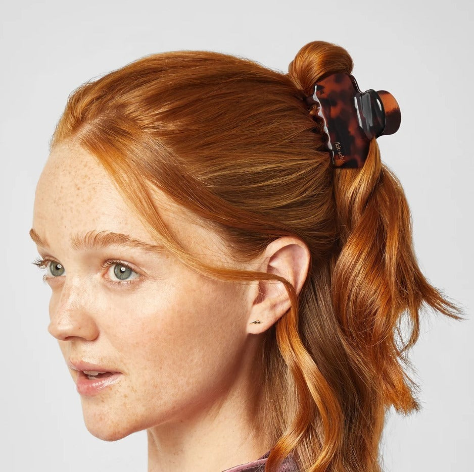 Person with red hair tied in a ponytail using a tortoiseshell hair clip on a light gray background