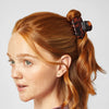 Person with red hair tied in a ponytail using a tortoiseshell hair clip on a light gray background