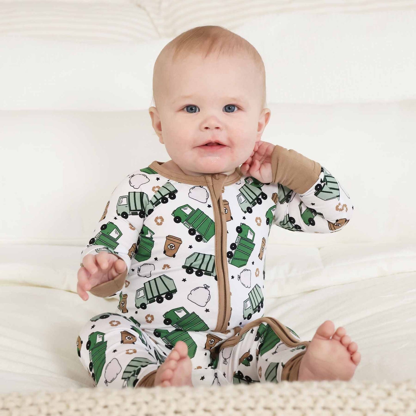 Baby wearing a onesie with green truck pattern on a white background