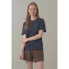 A woman modeling a dark slate blue short-sleeve t-shirt and brown shorts against a solid light gray studio background.