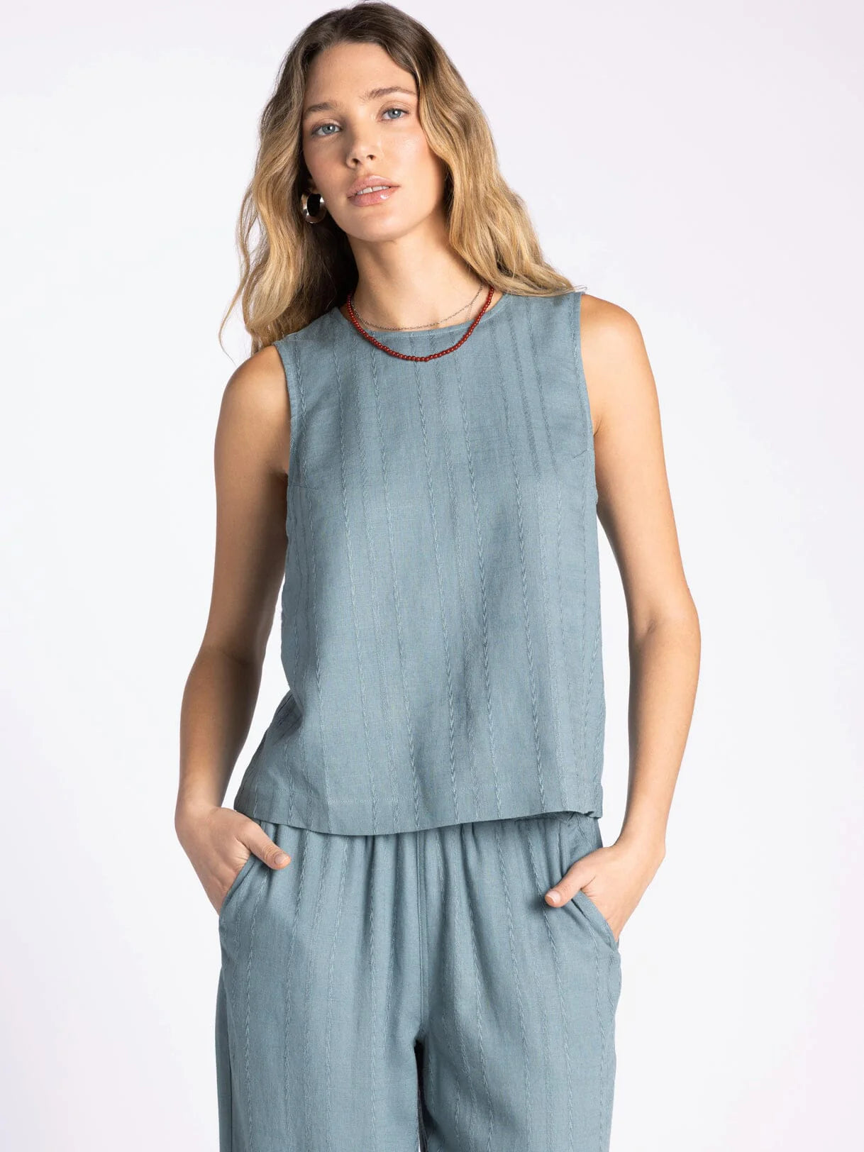 Woman wearing a light blue sleeveless top and pants on a white background