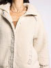 Close-up of a person wearing a beige fleece jacket with lace detailing on a light gray background