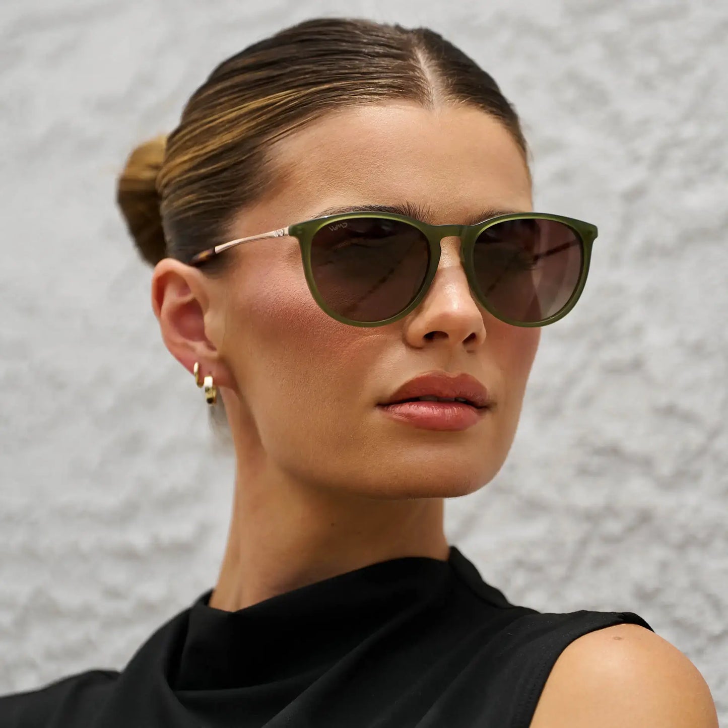 Woman wearing green sunglasses against a textured gray background