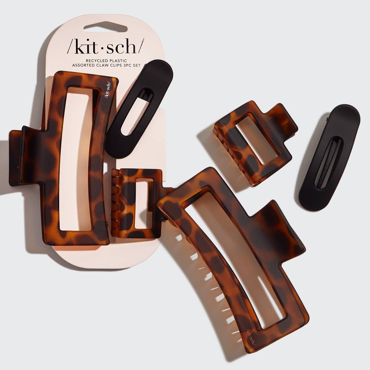 A Kit & Sch recycled plastic assorted claw clip set, featuring three brown tortoiseshell hair clips and two matte black clips, with one set displayed on its original packaging and the other set arranged flat on a light gray background.