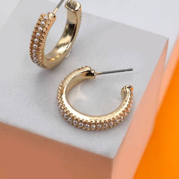 Gold hoop earrings with pearl-like beads on a light gray surface.