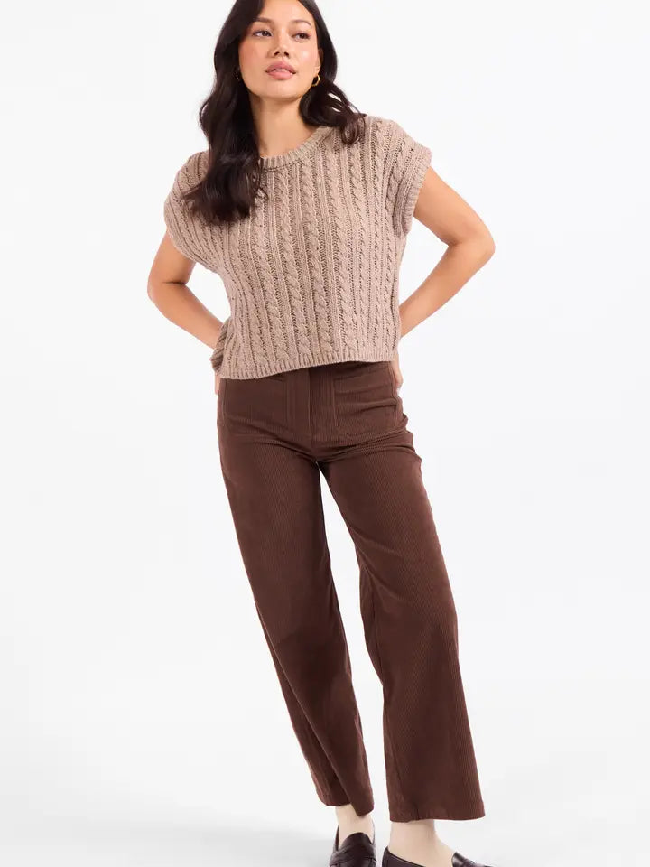 A woman modeling a beige cable-knit cropped sweater and brown wide-leg pants against a plain white studio background.