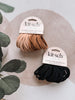 Two packages of kit-sch hair ties, one black and one brown, on a neutral background with green leaves.