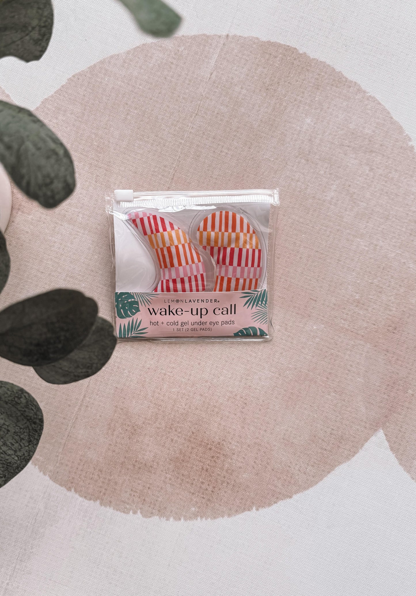 Packaged eye pillows with a tropical design on a pink circular mat.
