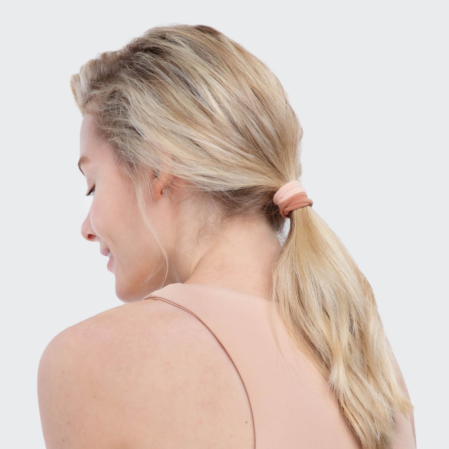 Woman with blonde hair tied in a ponytail with a pink hair tie on a white background