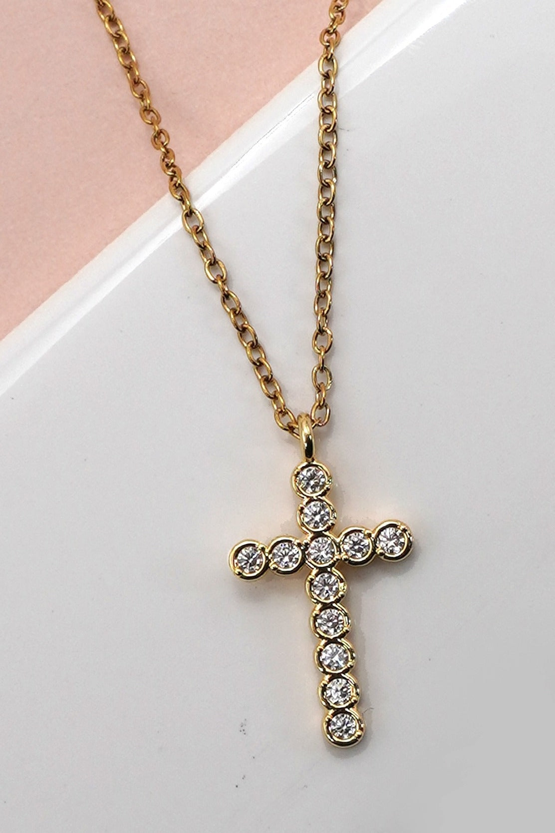 Gold cross necklace with clear stones on a white surface