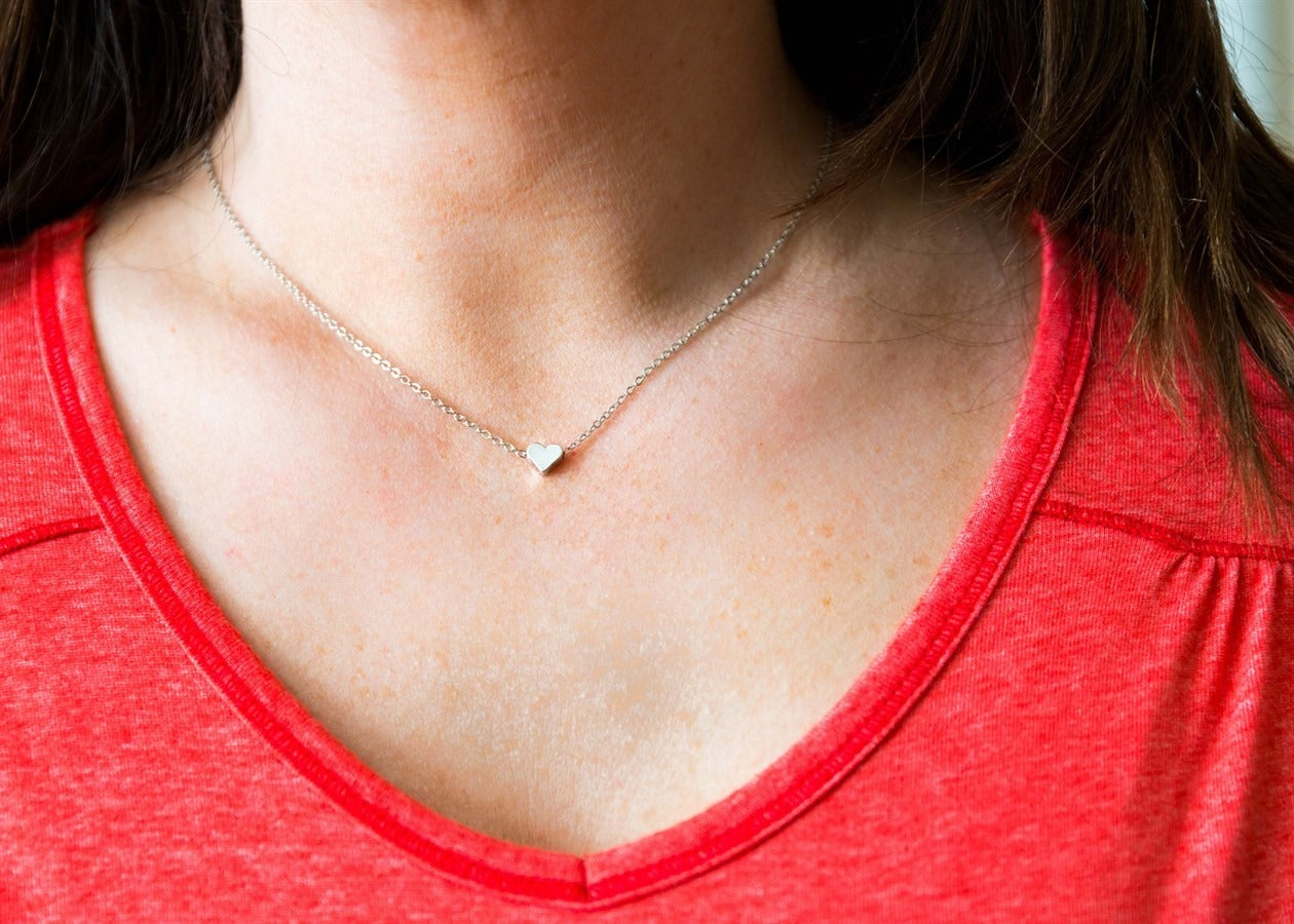 Person wearing a red shirt and gold necklace with a heart pendant