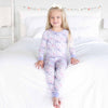 Young girl wearing a floral pajama set sitting on a bed.